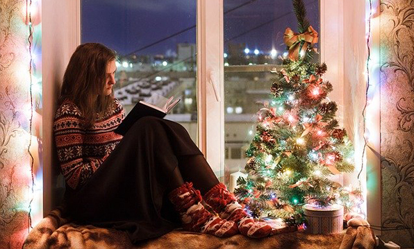 Girl sitting on a window sill filled with Christmas decorations